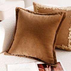 two brown pillows sitting next to each other on a white couch with an open book