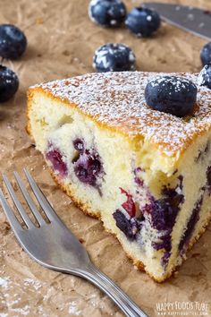 a piece of cake with blueberries and powdered sugar on top next to a fork