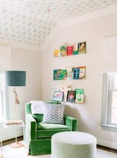 a green chair and ottoman in a small room with white carpeted flooring, two windows, and wallpaper on the walls