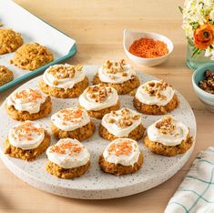 a white plate topped with cookies covered in frosting next to bowls of nuts and carrots