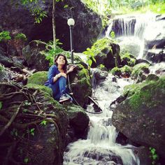 a woman sitting on the rocks next to a waterfall with a lamppost in her hand