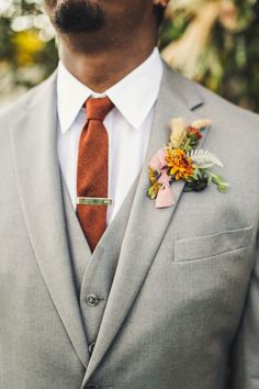 a man wearing a gray suit with a red tie and flower boutonniere