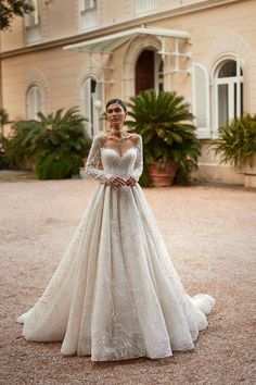 a woman standing in front of a large building wearing a wedding dress with long sleeves