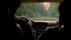 two people sitting in the passenger seat of a car, looking at something on the dashboard