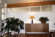 a living room with plants and a lamp on top of the dresser in front of it