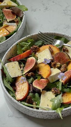 two bowls filled with fruit and cheese on top of a white countertop next to a fork