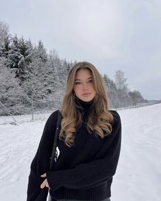 a woman standing in the snow with her arms crossed and looking off to the side