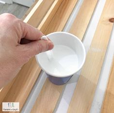 a hand is holding a cup with something in it on top of a wooden table