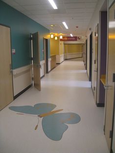 an empty hospital hallway with blue and yellow walls, white floors and light wood doors