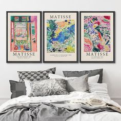 three posters on the wall above a bed in a room with white walls and pillows