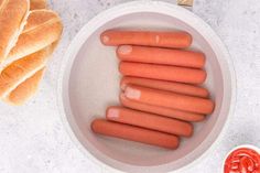 several hot dogs in a bowl next to some bread