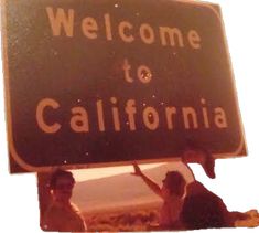 two people holding up a welcome to california sign