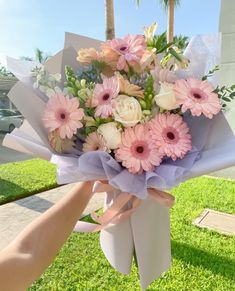 a bouquet of flowers is being held up by someone's hand on the grass