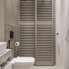 a white toilet sitting in a bathroom next to a walk in shower and wooden slatted doors