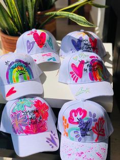 six hats with different designs on them sitting next to a potted plant