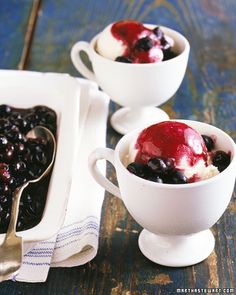 two white bowls filled with blueberries and ice cream on top of a wooden table