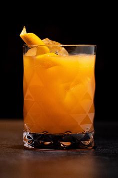 a glass filled with an orange drink on top of a table