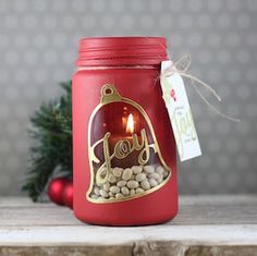 a red mason jar filled with nuts and a lit candle that says joy on it