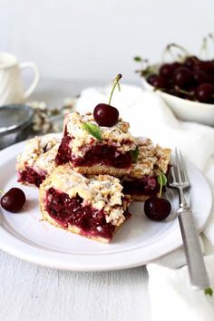 two pieces of cake on a plate with cherries and a fork next to it