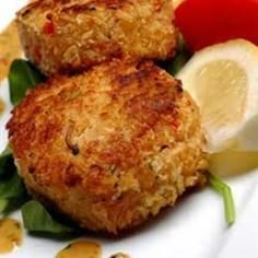 two crab cakes on a plate with lemon wedges