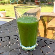 a glass filled with green liquid sitting on top of a table next to a bench