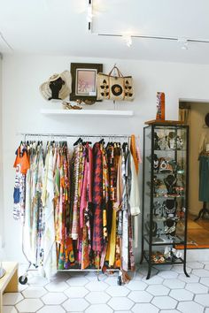 a clothing rack filled with clothes next to a mirror and shelf full of other items