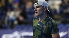 a male tennis player in a green shirt and white hat