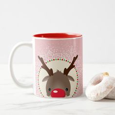 a coffee mug with a reindeer face on it next to a donut