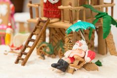 there is a miniature santa clause sitting on a chair under an umbrella in the snow