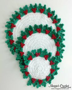 two crocheted placemats with red and green flowers on them, one is white and the other is green