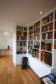 a living room filled with lots of books on top of a hard wood floor next to a white wall