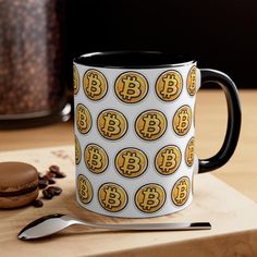 a bitcoin coffee mug sitting on top of a table next to a spoon