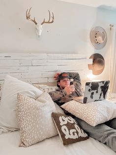 a man laying in bed with his laptop on his lap and deer head mounted to the wall behind him