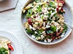 a salad with spinach, feta cheese and tomatoes in a bowl on a table