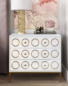 a white dresser with gold circles on the drawers and a painting above it in a living room