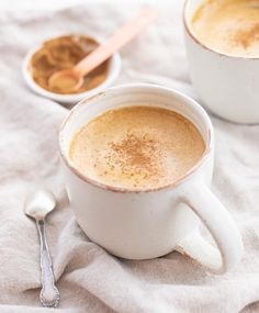 two cups of hot chocolate on a white cloth with spoons next to one cup