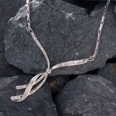 This bejeweld 14k white gold necklace features a ribbon motif accented with one (1) bezel set round brilliant cut diamond, thirty-nine (39) prong set round brilliant cut diamonds, and thirty-five (35) channel set baguette cut diamonds. The pendant measures 57mm by 52mm and is attached to a fancy link chain.  The overall length of the necklace is 17.5 inches. Fine Jewelry Diamond Necklace With Channel Set, Formal White Gold Channel Set Necklace, Formal Diamond White Channel Set Necklace, Luxury Diamond Necklace With Channel Set, Diamond White Channel Set Necklace For Formal Occasions, Elegant Silver Diamond Necklace With Pavé Setting, White Gold Necklace With Pave Setting For Evening, Elegant White Gold Diamond Necklace Channel Set, Elegant White Gold Diamond Necklace With Channel Set