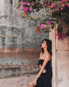 a woman leaning against a wall with pink flowers on the top and bottom of her head