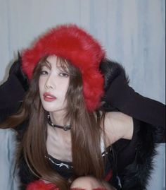 a woman with long brown hair wearing a red fur hat and black top sitting on a chair