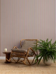 a rocking chair next to a potted plant in front of a striped wallpaper