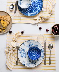 two plates with blue and white designs on them are next to forks, spoons and bowls