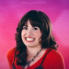 a woman with long dark hair smiling at the camera while wearing a red shirt and necklace