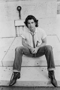 black and white photograph of a man sitting on steps with his legs crossed wearing a tie