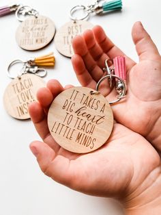 a hand holding a wooden keychain that says it takes a big heart to teach little minds