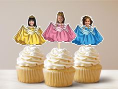 three cupcakes with white frosting and princess cutouts on top, sitting next to each other