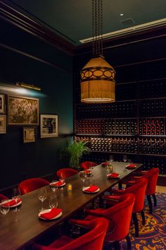 a long table with red chairs and wine bottles on the wall in front of it