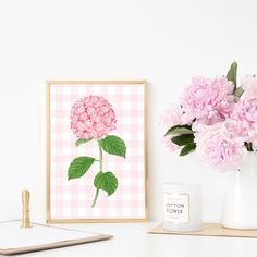 a pink flower is in a vase next to a white mug and framed photograph on a table