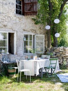 an outdoor table and chairs in front of a stone house