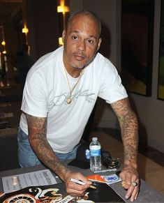 a man sitting at a table with some tattoos on his arm and hand holding a pen