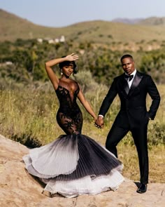 a man and woman in formal wear holding hands while standing on top of a hill